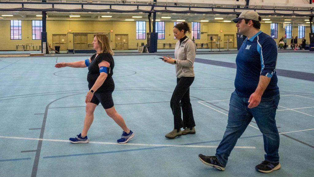 A photo of a research subject walking with researchers in UMaine's Field House
