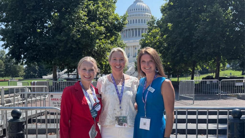 Three people smile and pose for a photo outside of the U.S. Capital Building in Washington, D.C.