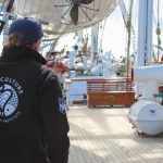 A photo of a person wearing a UMaine Aquaculture Research Institute jacket on the deck of a tallship